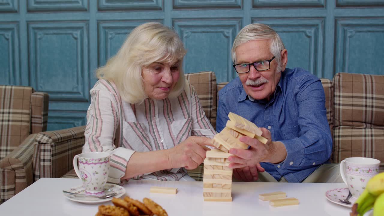 una pareja de ancianos, abuelo y abuela, descansando en el sofá, jugando a un juego con bloques de madera en casa.