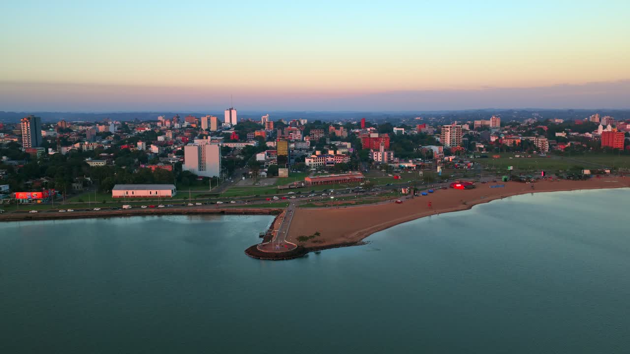 Ampio panorama aereo con drone della Spiaggia di San José, del molo e dello skyline della città lungo il fiume Paraná al tramonto a Encarnación, Paraguay.