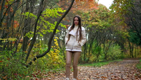 relaxed long-haired brunette tossing fallen leaves walking by the road. calming leisurely stride in the autumn park.