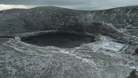 paisaje montañoso nevado con un lago oscuro y tranquilo y senderos sinuosos, tiempo nublado, vista aérea