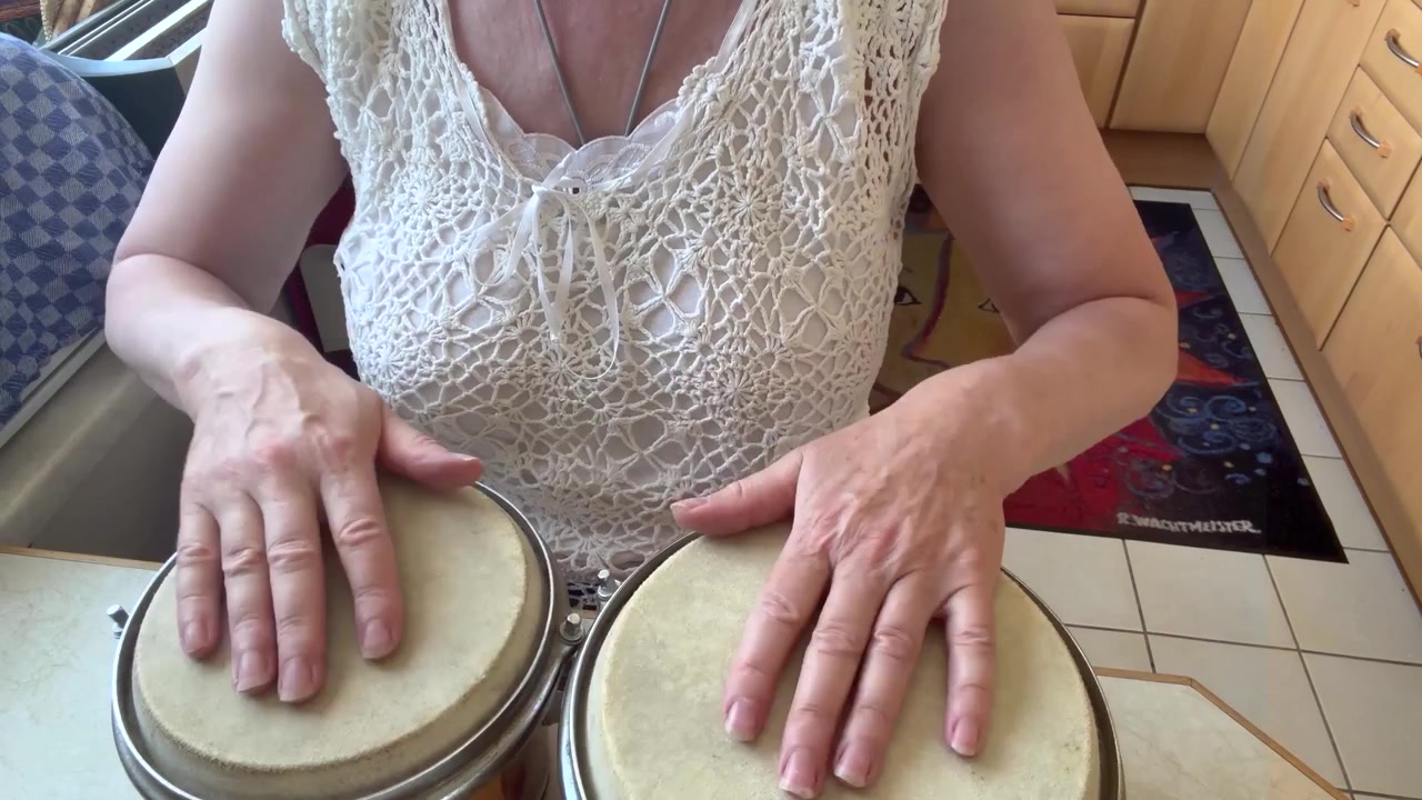 Uma mulher senta-se à mesa da cozinha tocando dois tambores de mão filipinos artesanais com peles de tambor de couro animal natural. Tomada estática média.