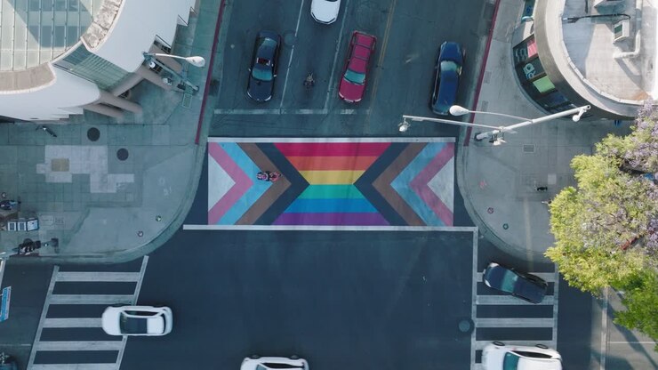 Imagens aéreas sobre um cruzamento com padrão colorido de arco-íris, carros virando e pedestres caminhando