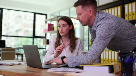 two colleagues collaborating and discussing work on a laptop in an office