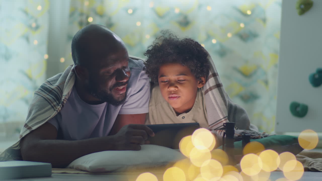 Papà e figlio afroamericani che usano un tablet la sera a casa
