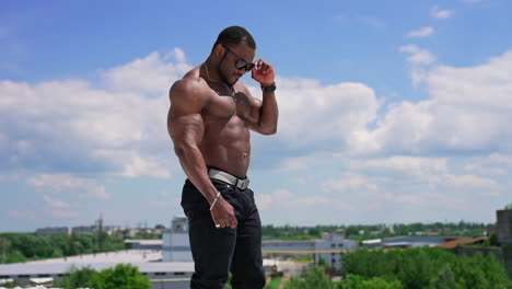 Portrait of handsome african sportsman outdoors. Cheerful shirtless athlete with strong trained muscles standing on the hill against blue sky.