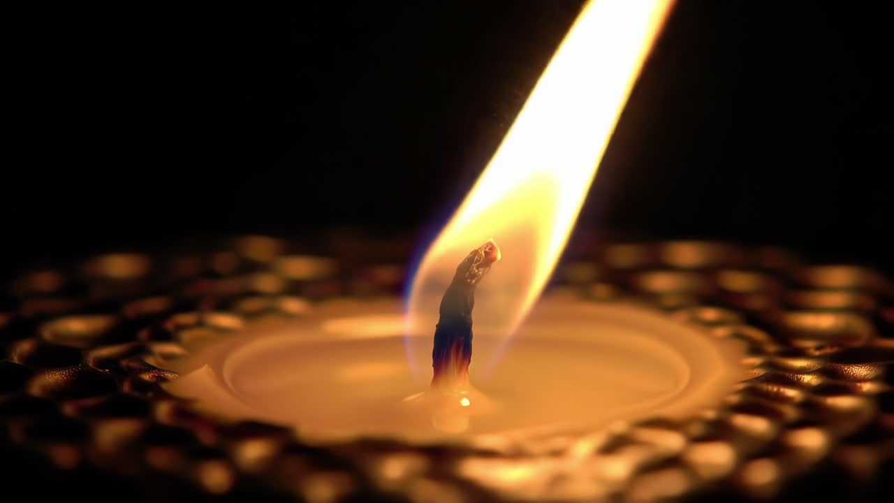 Fiamma incantevole: primo piano di uno stoppino di candela tremolante che illumina l'oscurità con il suo bagliore caldo in un ambiente sereno