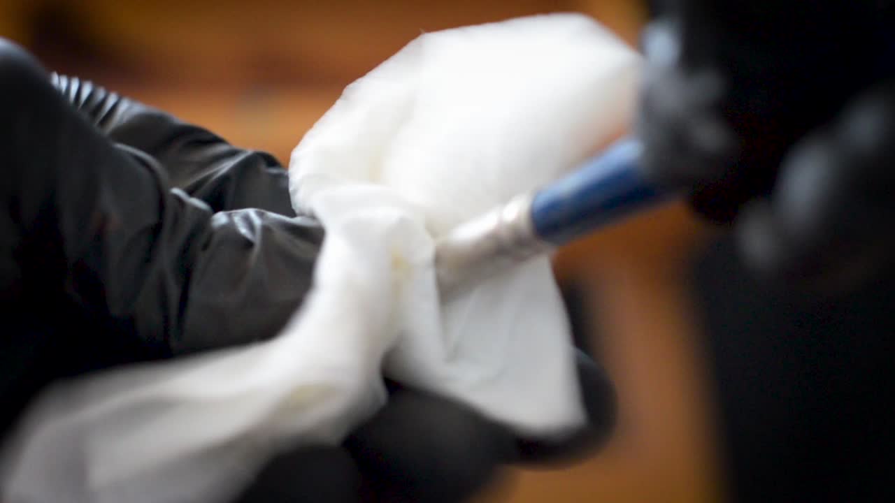 primer plano limpiando el pincel de pintura al óleo de un artista con una toalla de papel y guantes