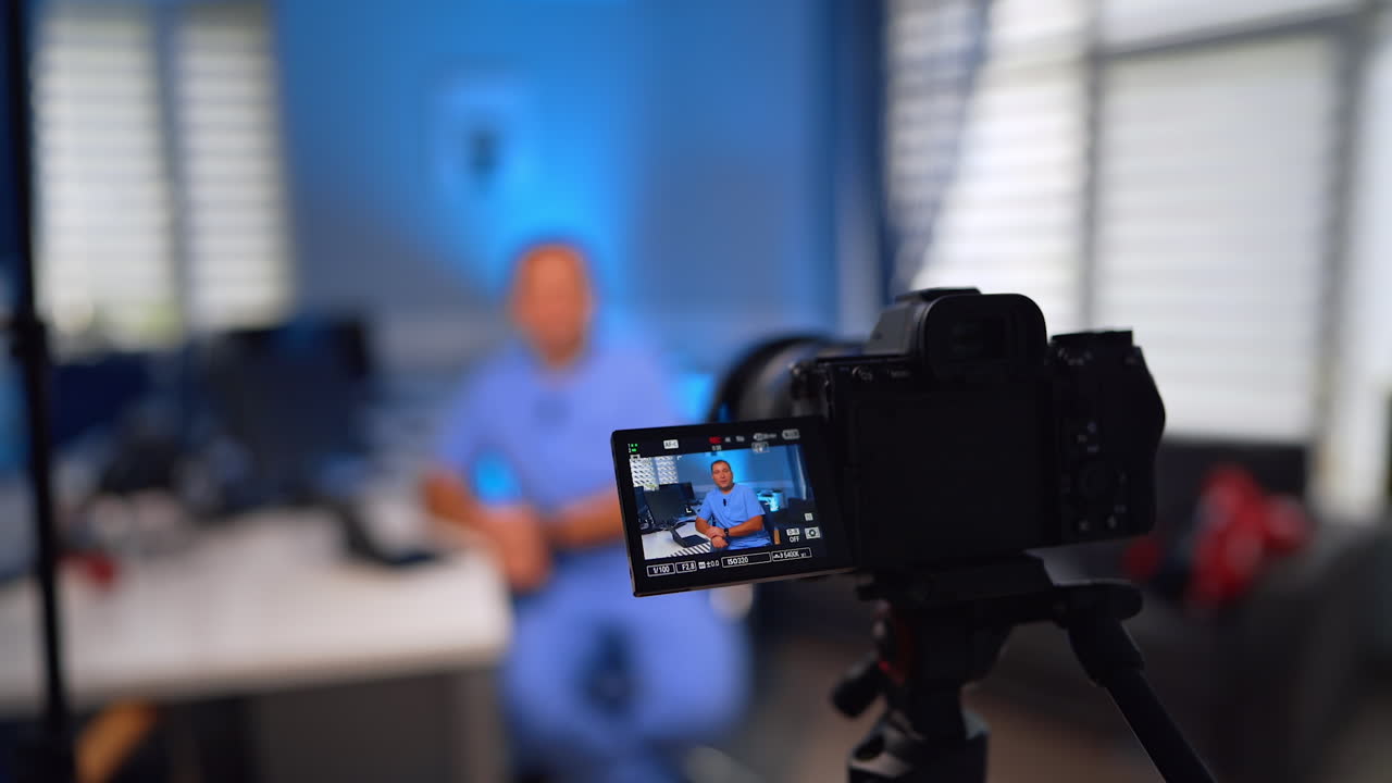 Professional male doctor in blue uniform sits ay desk talking to camera. Close up. Medical vlog concept. Selective focus