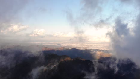 a heavenly paradise of mountains covered with white clouds underneath a vibrant early morning sunrise - aerial shot