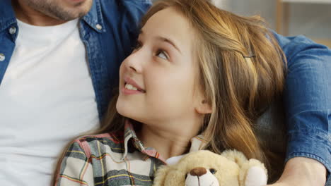 close up of the teenage cute blonde girl sitting and hugging her teddy bear while her father hugging her