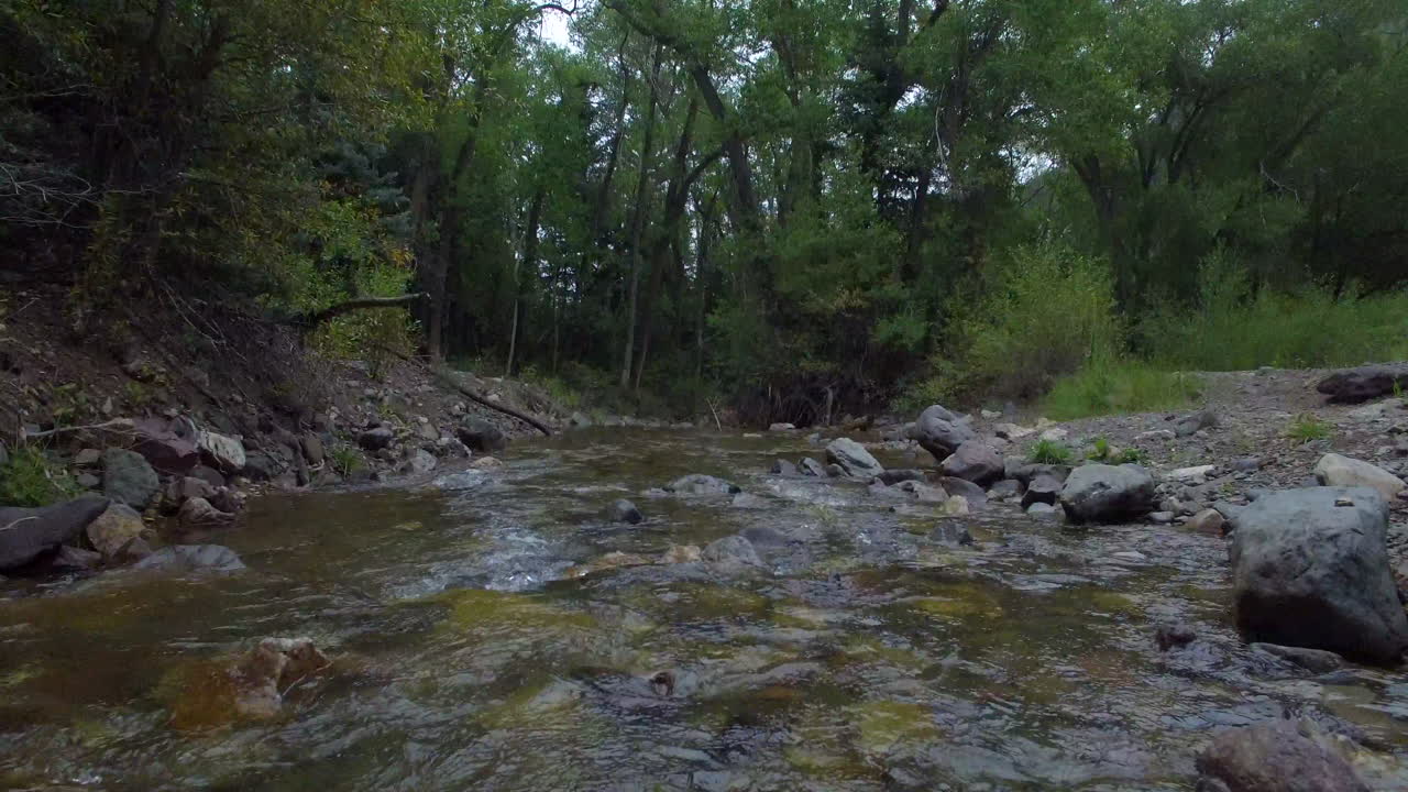 lento, avión no tripulado de bajo vuelo disparado sobre un tranquilo arroyo que fluye hacia algunos árboles verdes