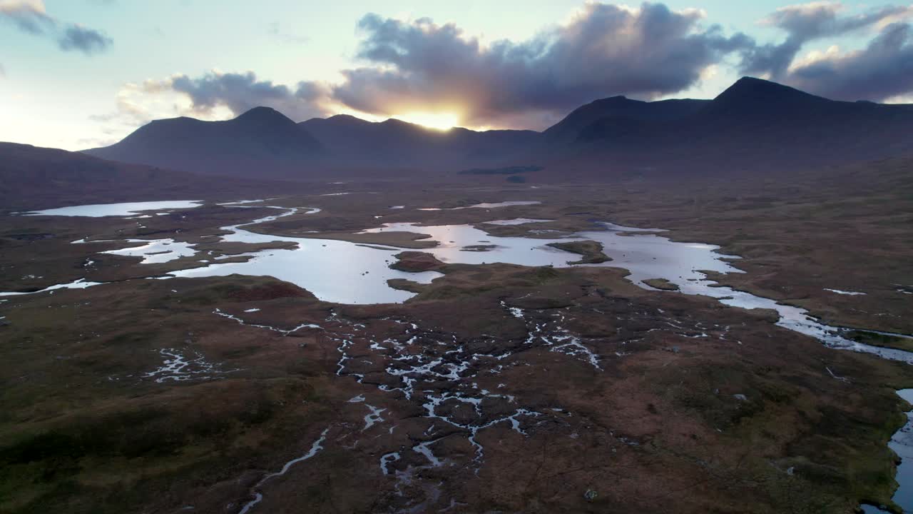 un dron rodando lentamente sobre un paisaje de humedales de islas y turberas rodeadas de agua dulce mientras mira hacia las montañas oscuras al atardecer