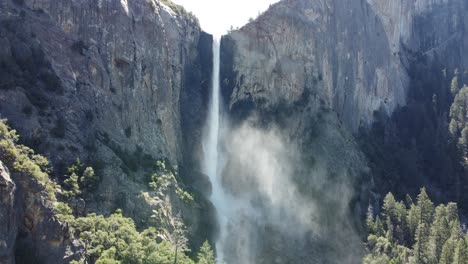 sunlight illuminating a cascading waterfall spraying mist into the mountain, forest, and valley of yosemite national park, california, usa.