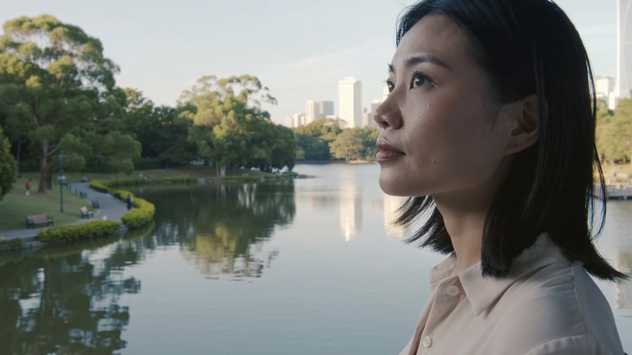 穿着衬衫的女人最初向下凝视，随后抬眼向上，观察公园湖泊的天际线，留有文案空间。