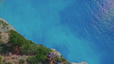 aerial panning down to people near huge cliff over blue ocean on greek island