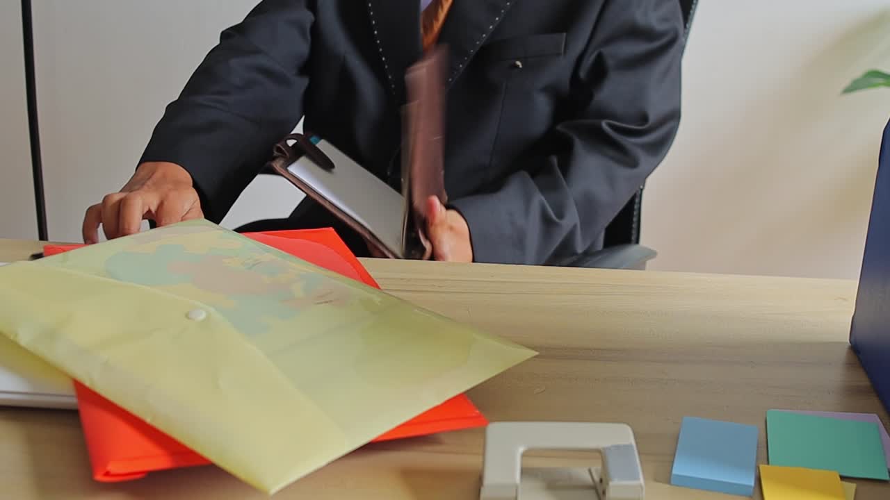 Businessman in suit opening leather planner at desk with office supplies
