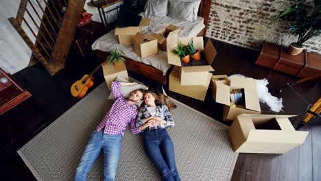 top view of attractive husband and wife lying on bedroom floor in new house and having conversation. young family, relationship and relocation concept.