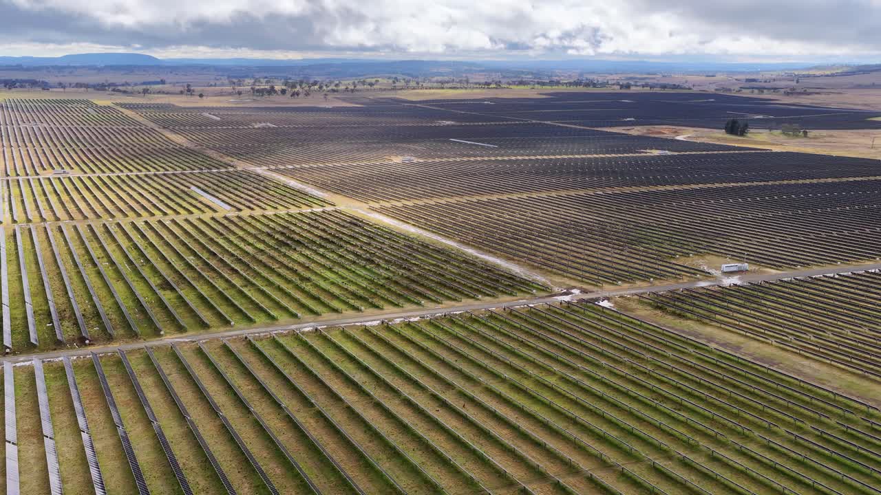 Drone glides above expansive solar panel array, cloudy sky, natural light, wide landscape view