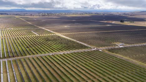 drone glides above expansive solar panel array, cloudy sky, natural light, wide landscape view