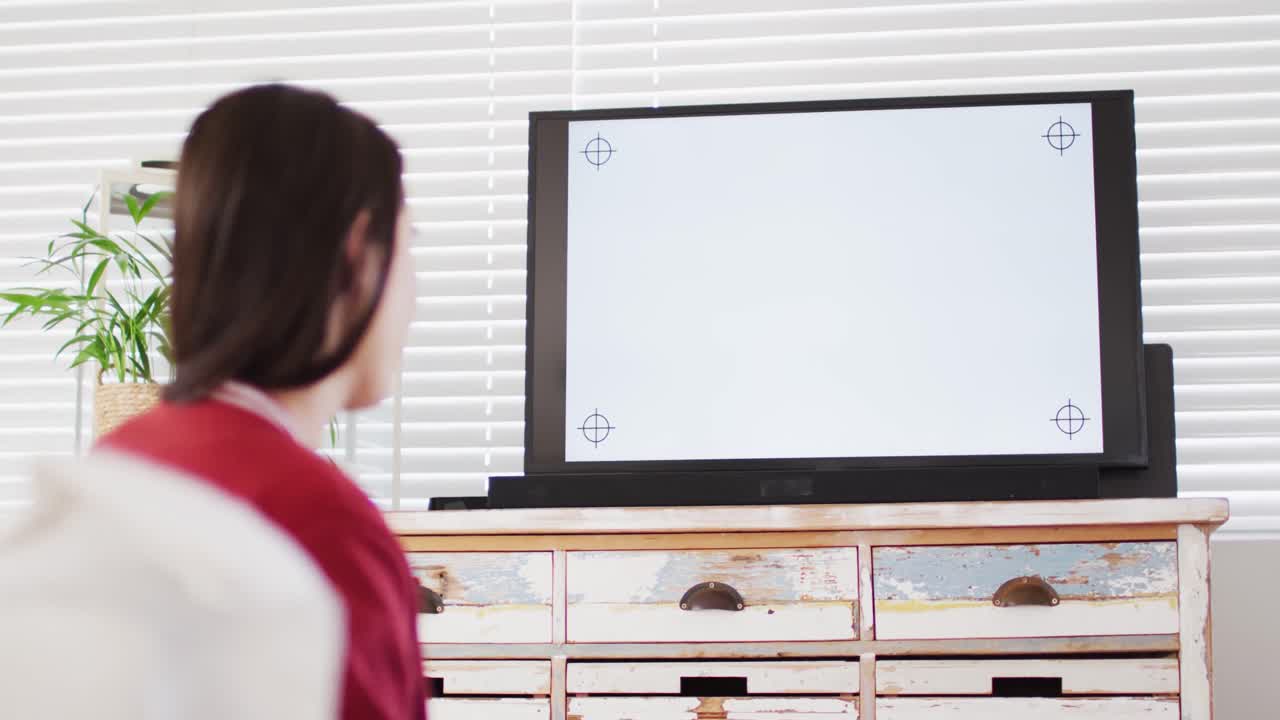 소파에 앉아 간식을 먹고 거실에서 복사 공간으로 tv를 보는 백인 여성