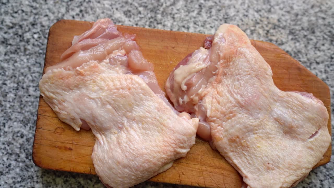 muslos de pollo crudos con piel en una tabla de cortar de madera