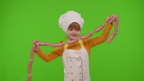 child girl dressed as cook chef in apron puts on a bunch of sausages around her neck, fooling around