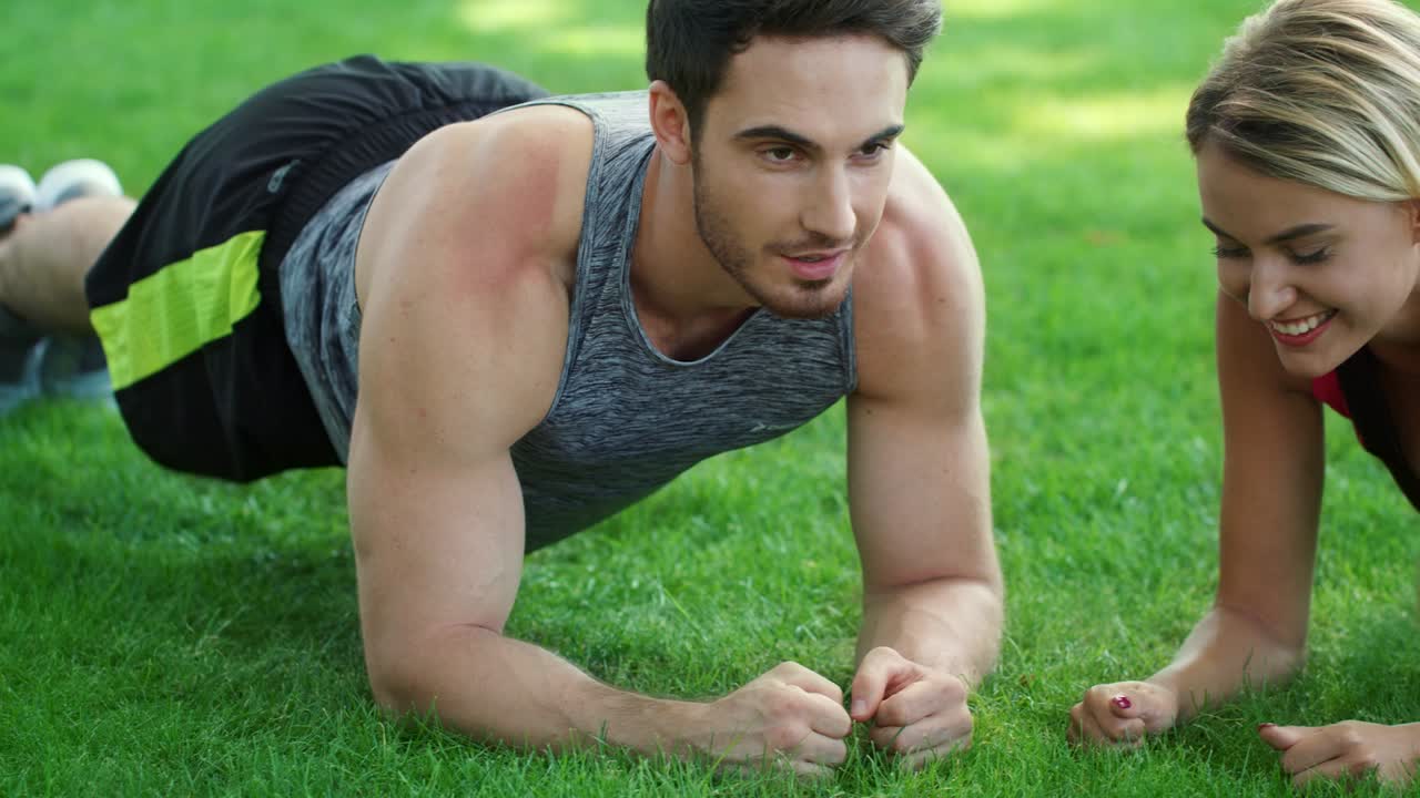 pareja feliz entrenando juntos ejercicio de tabla en el parque. tabla de pareja deportiva