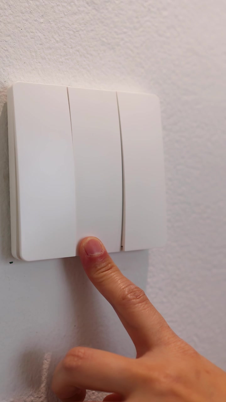 A person's finger presses three different buttons on a white light switch against a wall