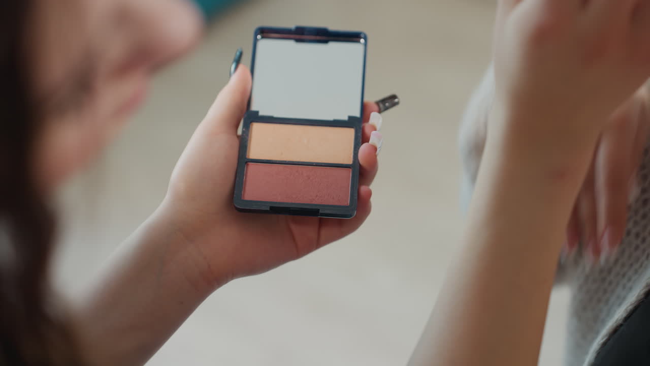 Compact Palette Held Between Hands, Friends Comparing Shades, Casual Consultation In Cozy Interior, Sweater Sleeve Visible, Tactile Swatch, Product Selection Moment, Lifestyle Beauty Scene