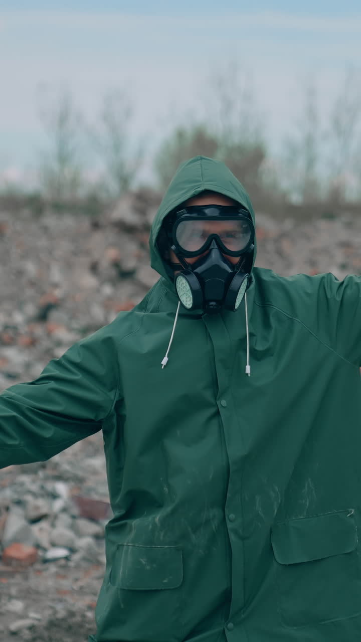 Man in safety suit and respirator on garbage background. Mad man in protective costume and gas mask dancing in abandoned place in radioactive zone. Vertical video