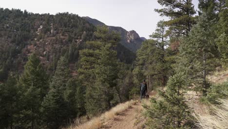 Hiker-with-backpack-walks-dog-on-leash-in-Colorado-mountain-forest