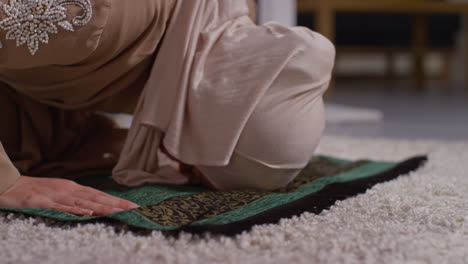 close up of muslim woman wearing hijab at home praying kneeling on prayer mat 7