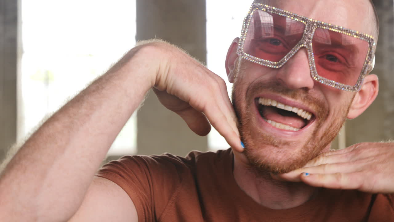Slow motion footage of a man in an industrial warehouse setting wearing rose tinted glasses smiling into camera.