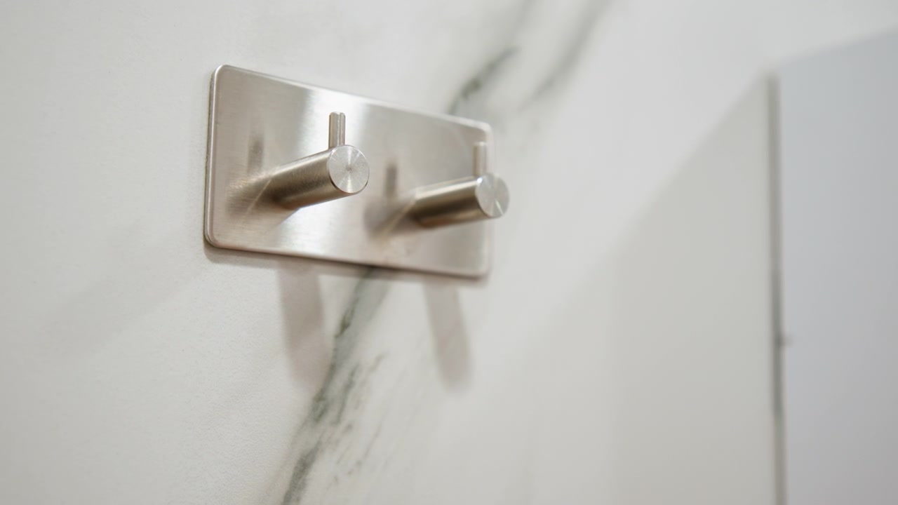 Chrome double hook on veined marble wall, revealing empty polished mount with reflective metal, subtle shadow, and clean modern interior texture in close low-angle view, with hook, chrome, marble