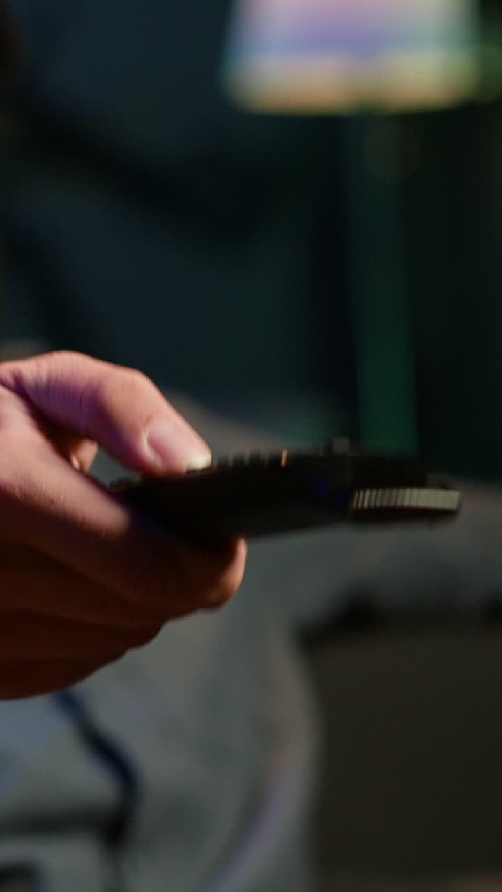 Vertical video Close up of remote used by man to scroll through TV channels