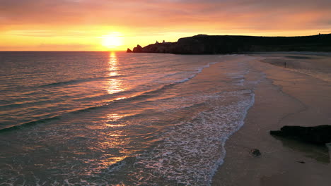 static aerial of sun setting over waves at beach with cliffs in the background