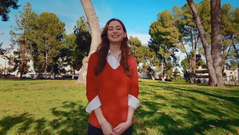 una feliz, atractiva, joven, mujer caucásica en el parque, se vuelve a la cámara y da una simple sonrisa