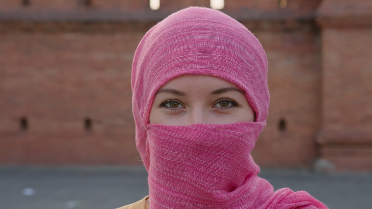 Woman wearing pink hijab in front of brick wall
