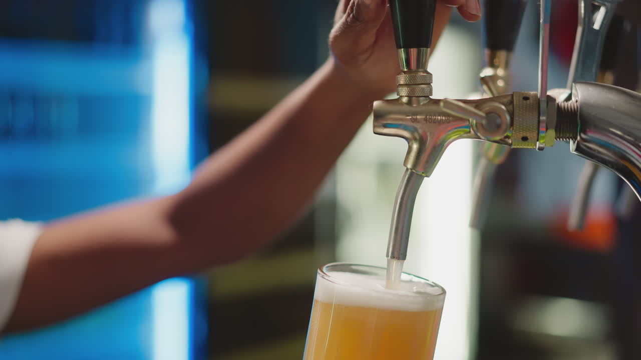 술집에서 컵에 맥주를 부는 술집장 - 아프리카계 미국인 술집장이 카운터에서 프에서 신선한 은 라거로 컵을 채니다. 흑인 남자가 카운터에서 일합니다.