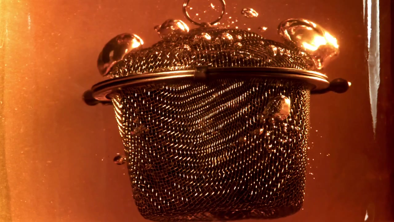 Primo piano di un infusore da tè che si immerge e infonde in un liquido caldo