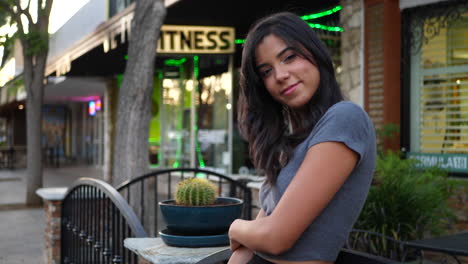 a beautiful hispanic woman consumer smiling and standing on the downtown urban city street full of shops and retail stores slow motion