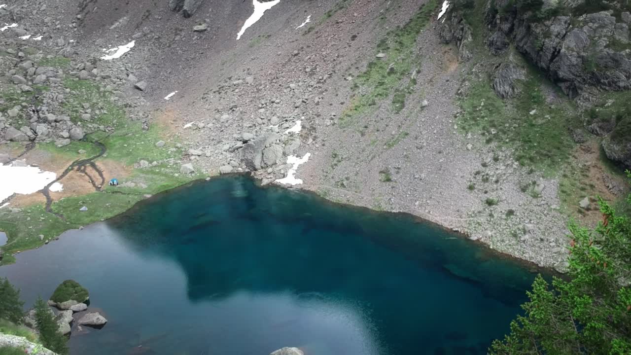 Volando sopra un bellissimo lago nelle Alpi italiane con una piccola tenda vicino alla riva.
