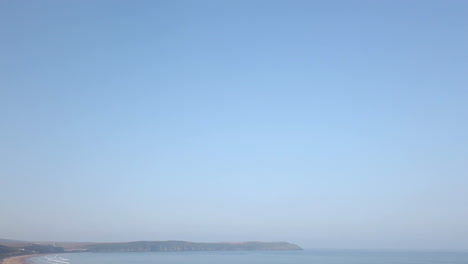 Wellen-Schlagen-Gegen-Einen-Langen-Sandstrand-In-Devon-Und-Verblassen-Im-Blauen-Himmel