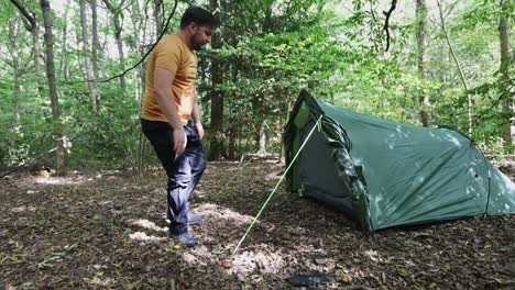 male traveler successfully finishes setting up a tent at the campsite in the woods