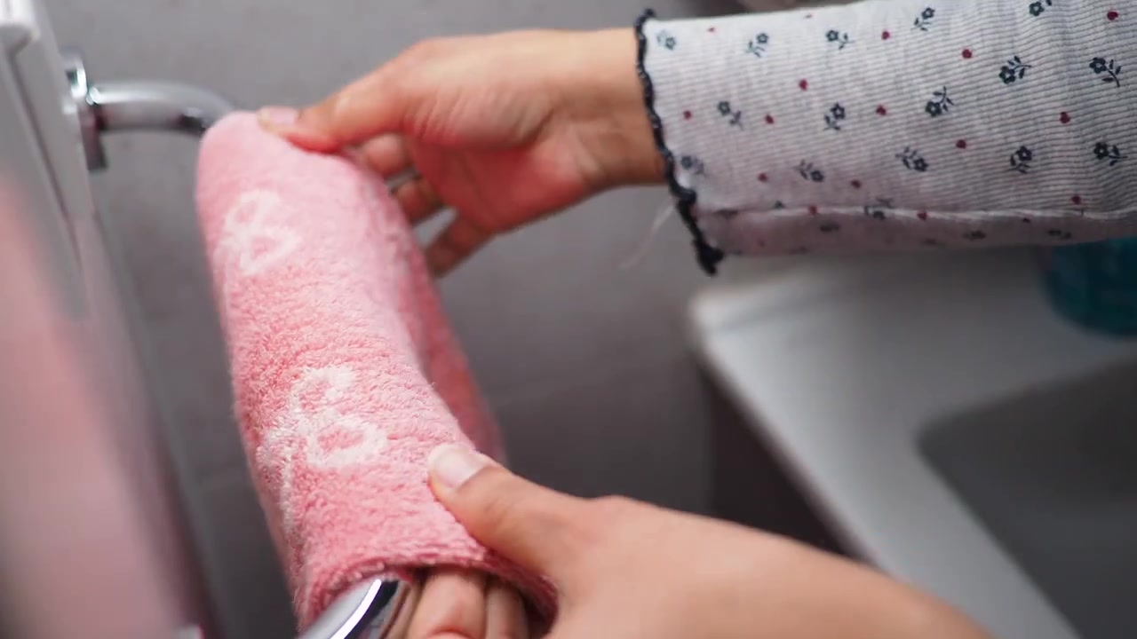 Mano di donna che appende un asciugamano rosa su una barra cromata in bagno