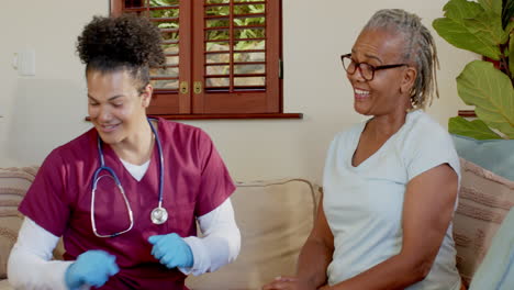 healthcare professional checking senior woman's arm at home, both smiling warmly