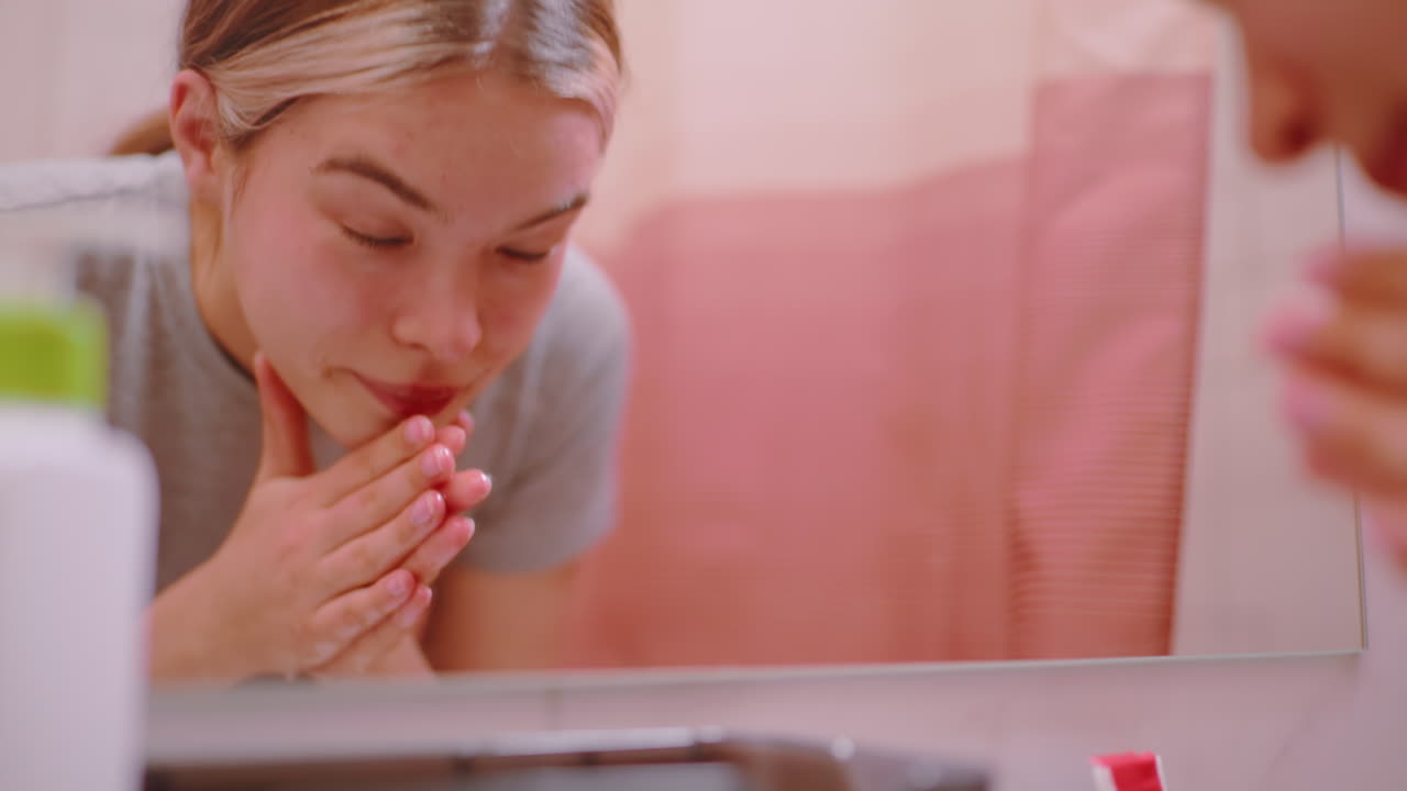 Close up of athlete washing face in bathroom sink after training, refreshing skin with water during skincare routine, showing tired expression and reflection in mirror with bathroom accessories