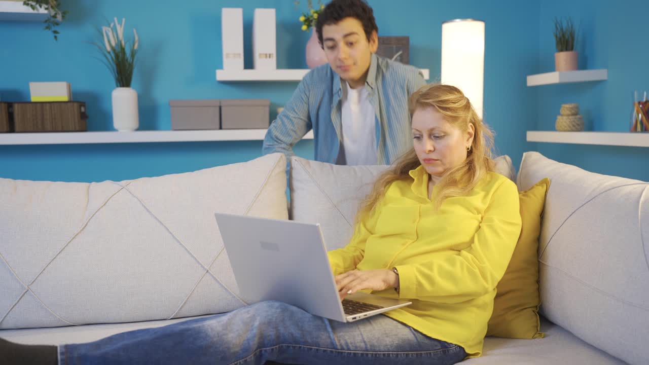 joven mirando a su madre que está mirando la computadora portátil. madre independiente.