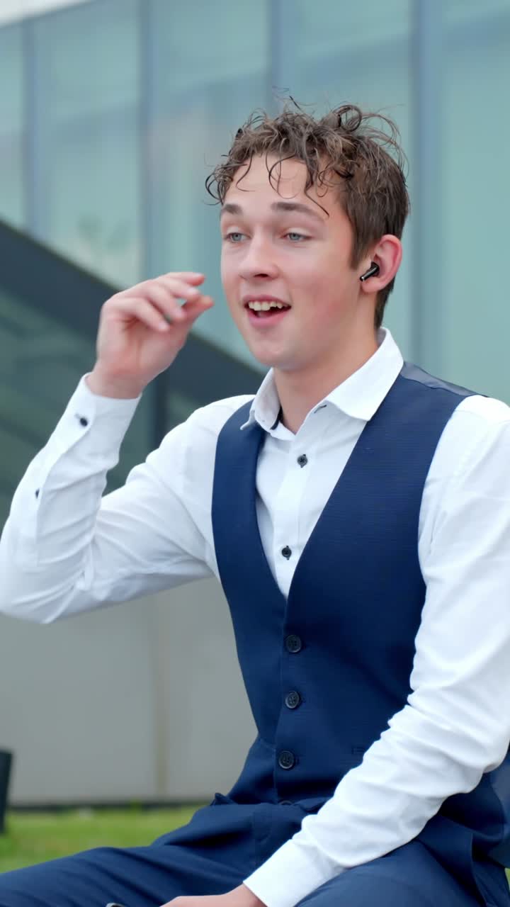 A Young Finance Analyst Appears Happy While Talking Through His Earpiece Outside the Office - Vertical Shot