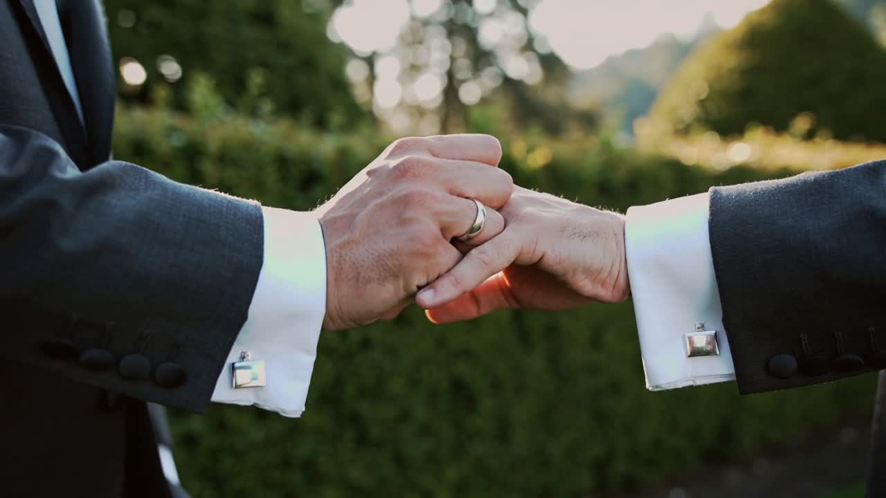 Sliding giver guiding gold band onto partner's left ring finger after vows at garden, cufflinks